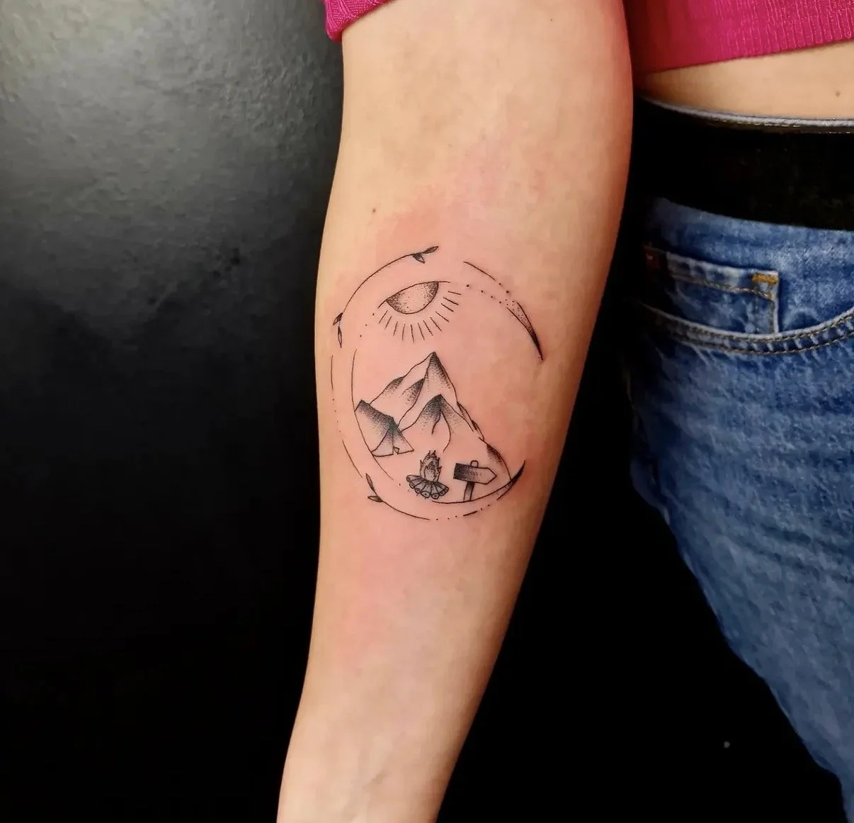 Tattoo auf dem Unterarm mit Berggipfeln, Mond, Sonne, Eule und Wegweiser, in minimalistischer Linienkunst.