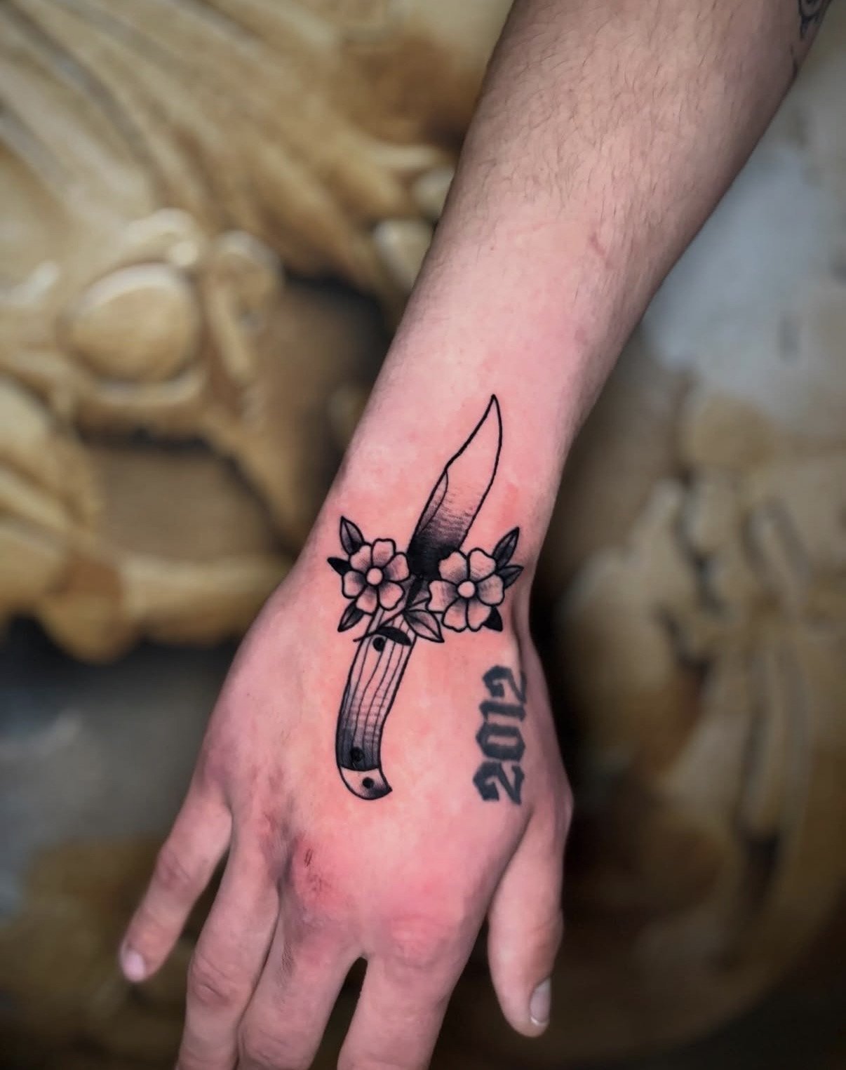 Tattoo eines Messer mit Blumen um den Griff auf dem Handgelenk