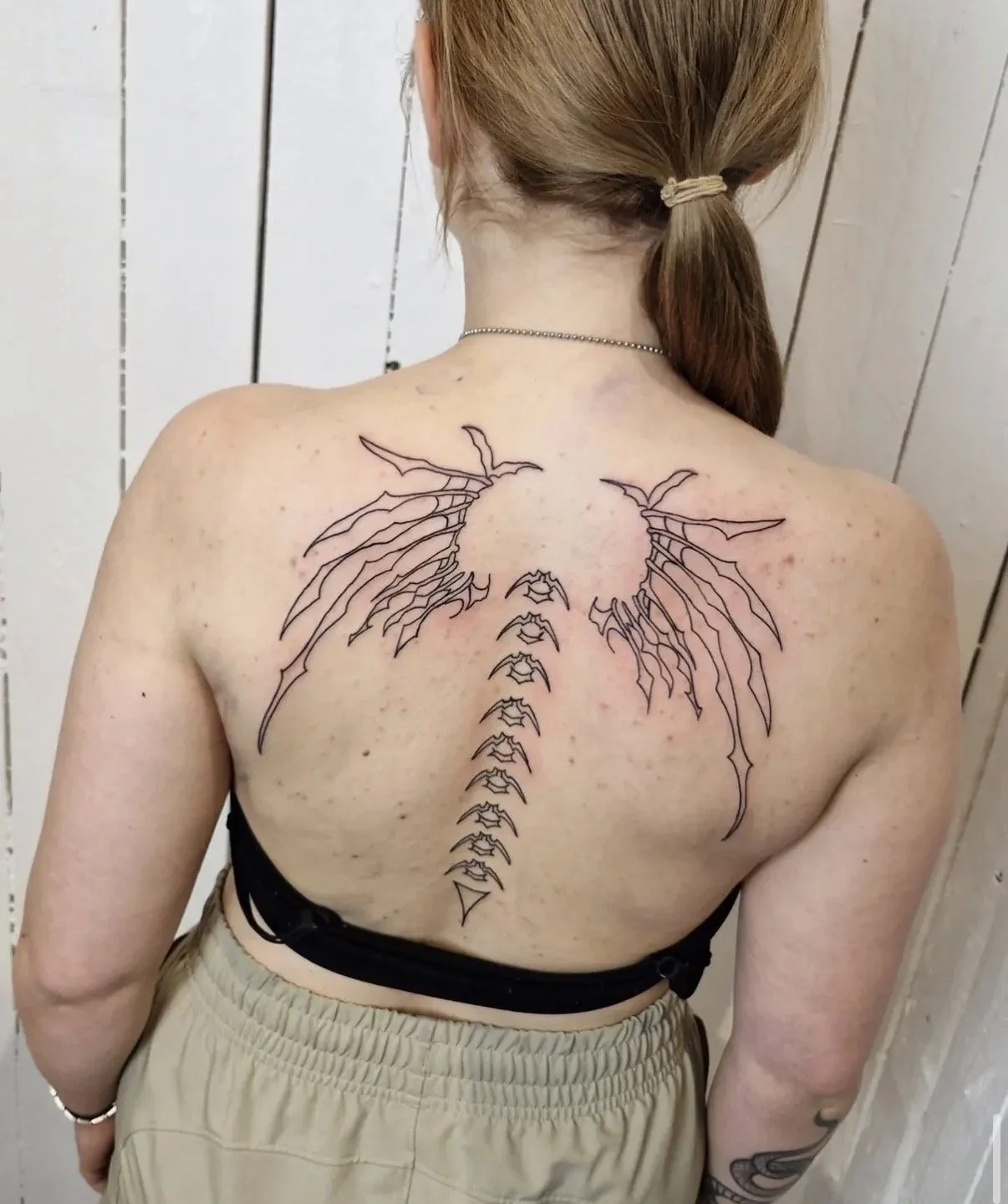 Vetower Kunstrissentattoo auf der Rückseite einer Frau, das Flügel und eine schwarze Linie enthält.