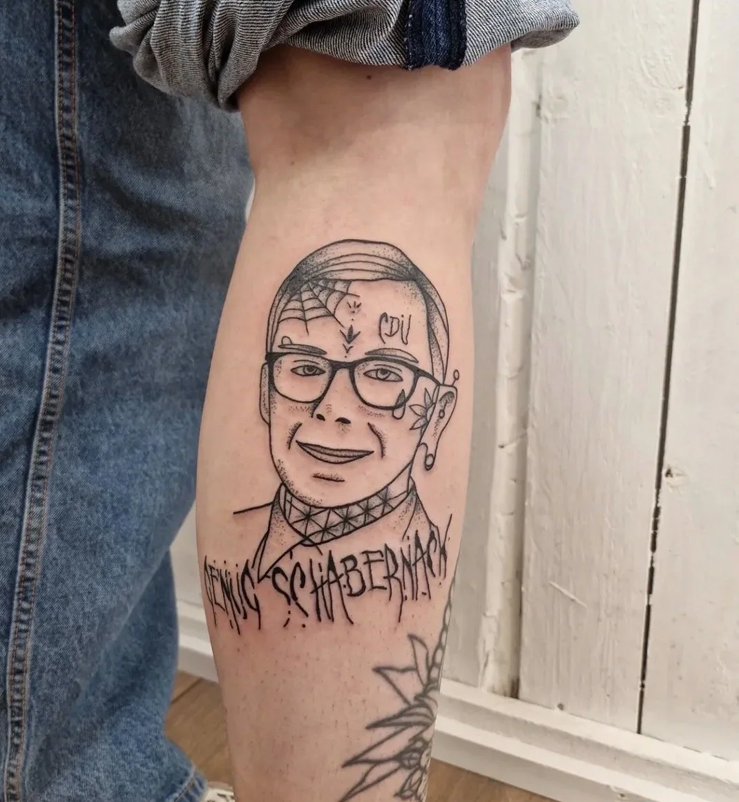 Tattoo eines Mannes mit Brille, Tattoo-Boxershorts, Tattoos auf Gesicht und Nacken, sowie der text "SPHABENADO" darunter auf dem Oberschenkel.