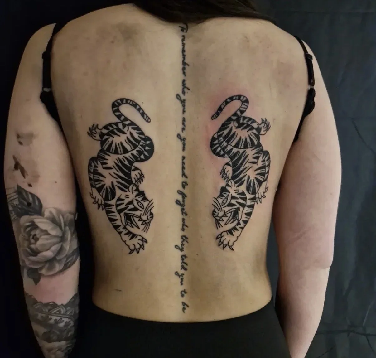 Tattoo auf dem Rücken mit zwei schwarzen Tigern und einer vertikalen Kette aus Texten.