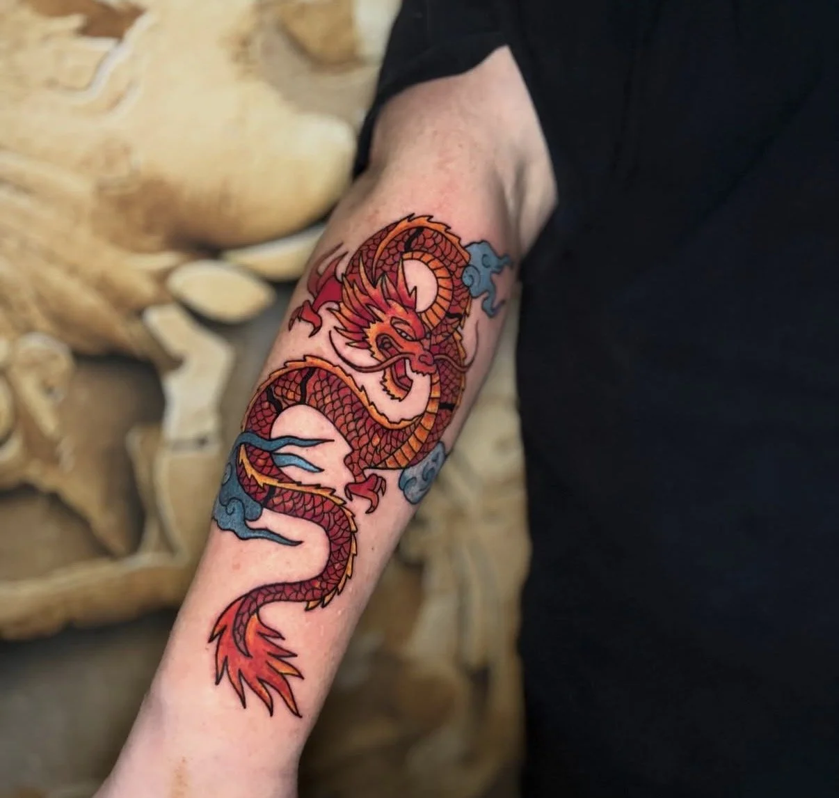 Tattoo eines roten Drachens auf dem Unterarm, umgeben von blauen Wolken und einer weißen Mondsichel.