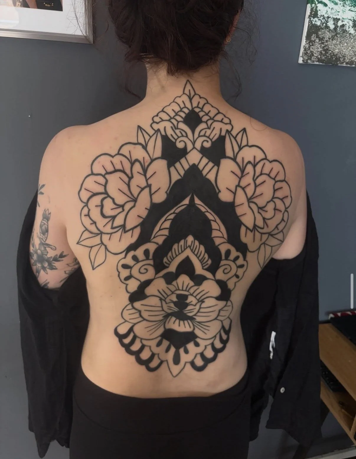 Großes schwarzes Tribal-Tattoo eines löwenkopfes, umgeben von Blumen, auf dem Rücken einer Person mit dunklen Haaren, die die Rückseite zeigt.