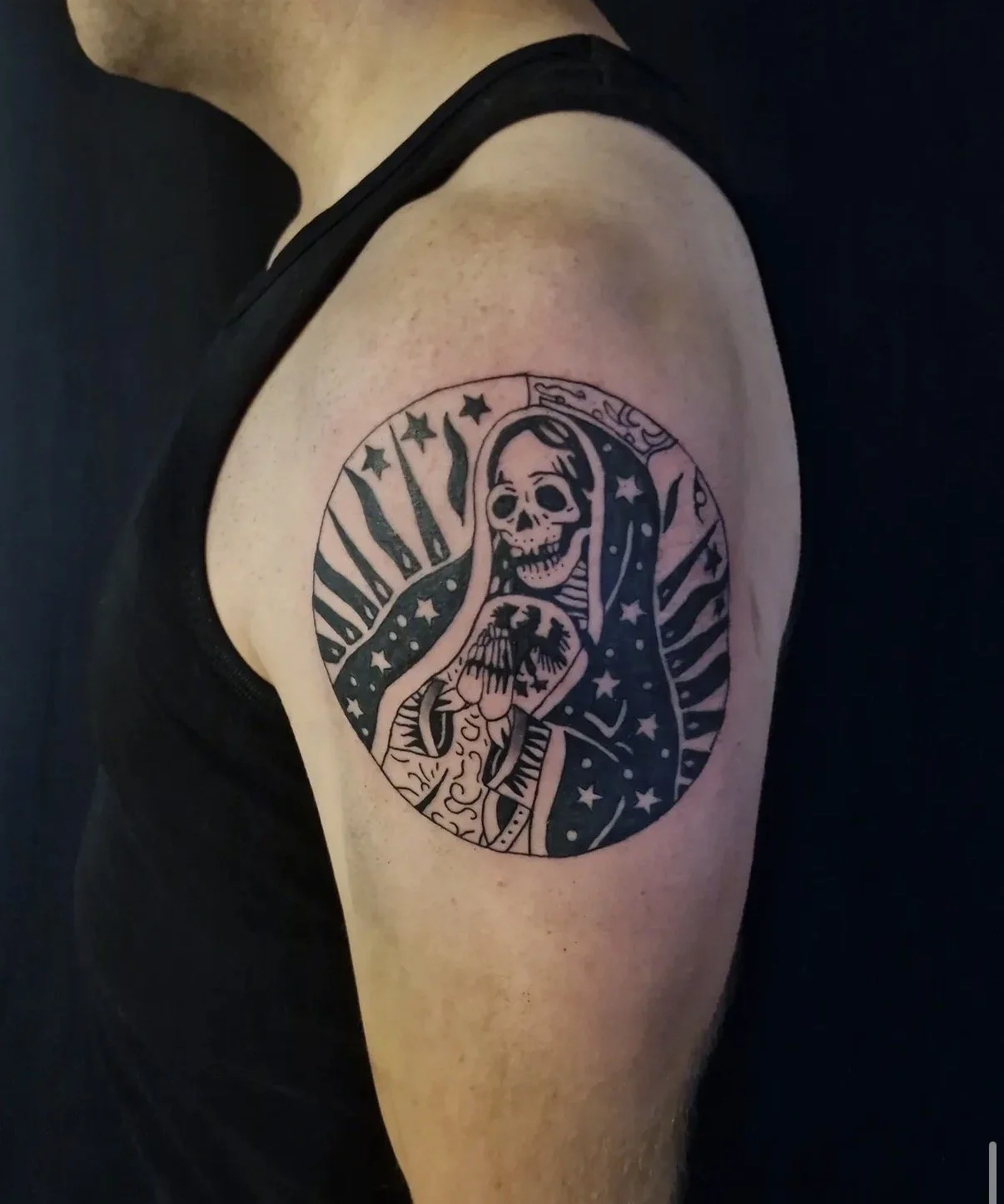 Schwarze Tattoo auf dem Oberarm, zeigt eine Skelettfigur mit Kapuzenmantel, umgeben von Sternen und Linien, im traditionellen Stil.
