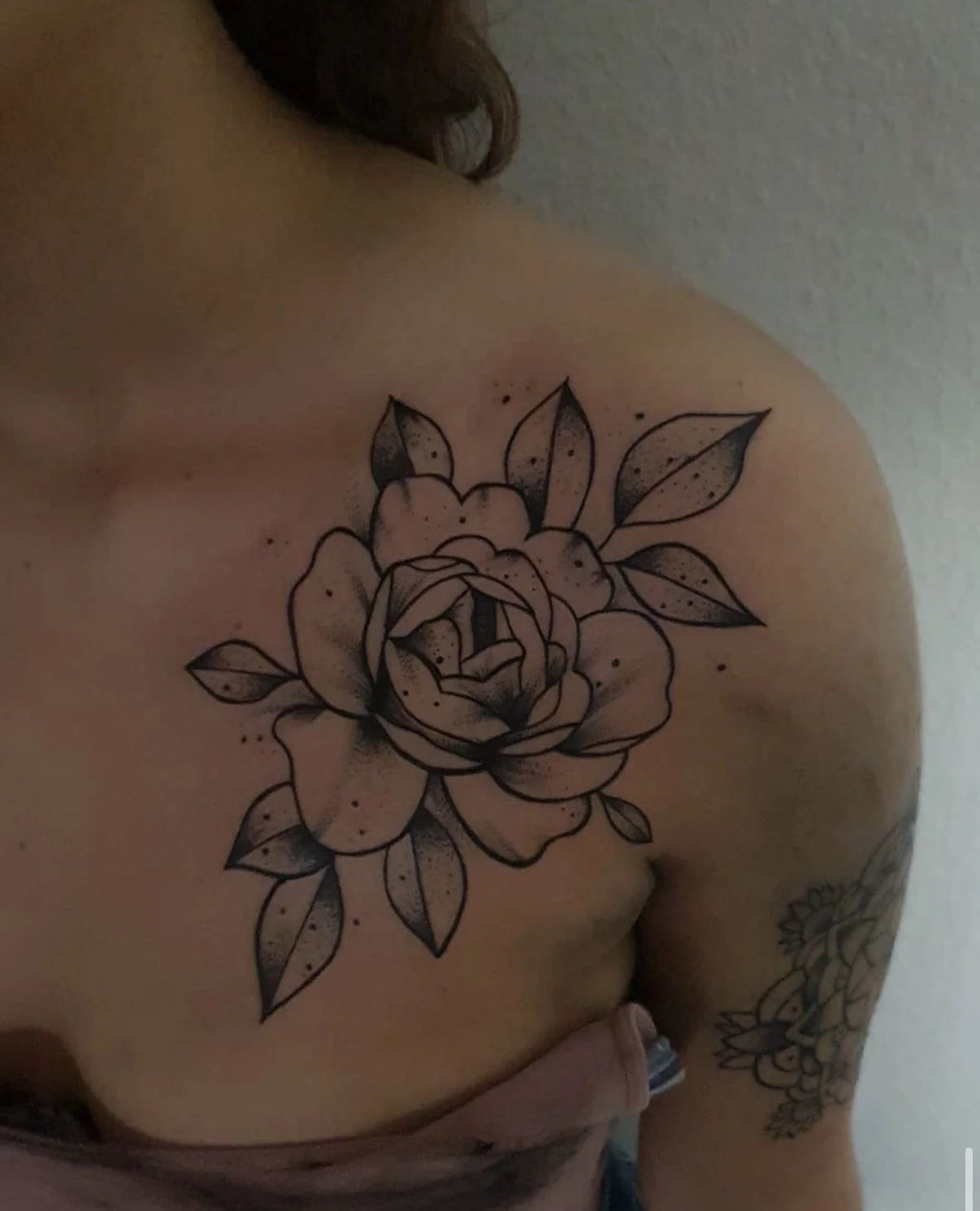 Schultertattoo eines stilisierten großen Rosenblumes mit Blättern in schwarzer Linienzeichnung auf der Haut einer Person.