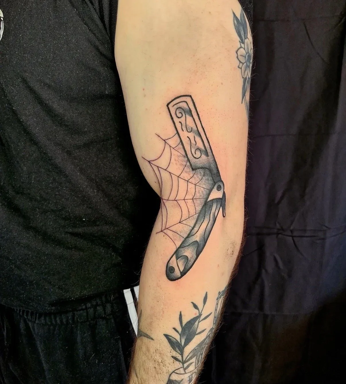 Tattoo eines Klappmessers mit Spinnenwebmuster auf dem Unterarm eines männlichen Menschen.