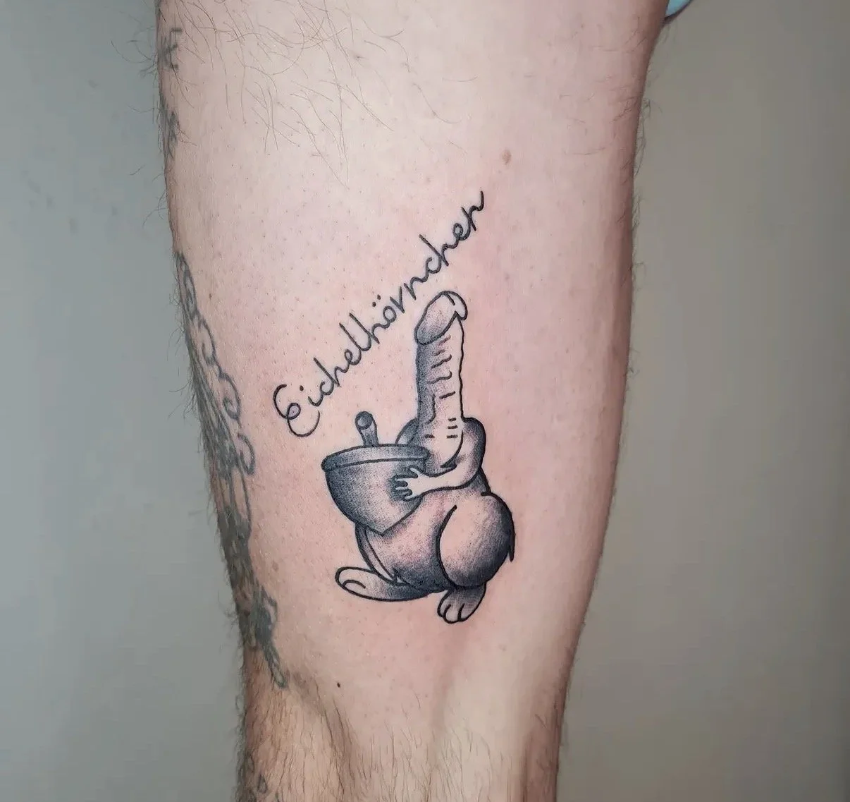 Tattoo eines Hundes, der eine Schüssel hält, mit dem Schriftzug "Eigenliebe" darüber.