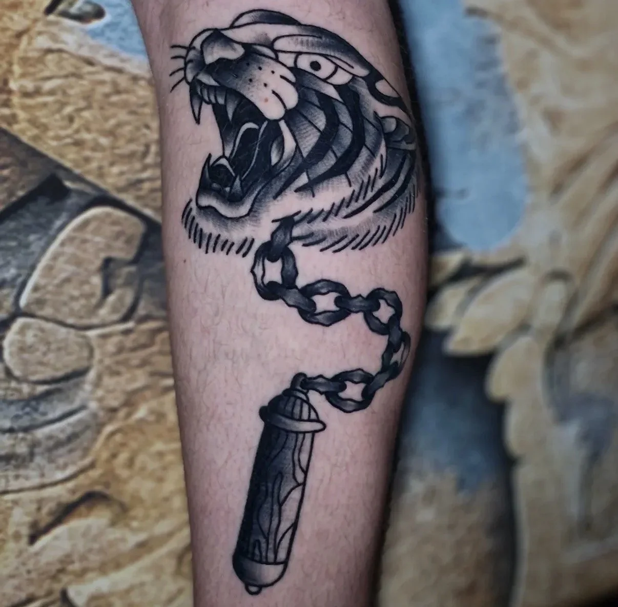 Tattoo eines löwenkopfes, der brüllt, mit einer Kette, die an einem Dynamitstift befestigt ist.