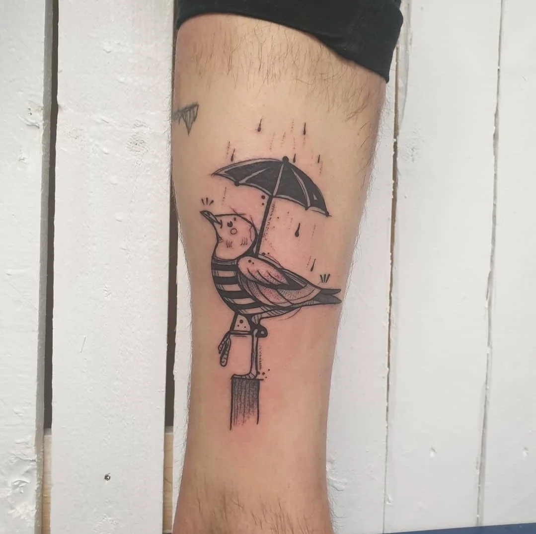 Tattoo eines vogels, das einen Regenschirm hält, auf einem Bein. Der Vogel trägt ein gestreiftes Hemd und hat einen kleinen Schnabel.