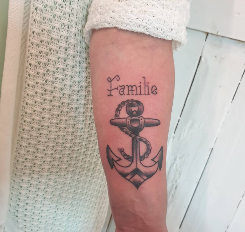 Eine Tätowierung auf einem Unterarm, bestehend aus einem Anker mit einer Kette und der Word "Familie" darüber.