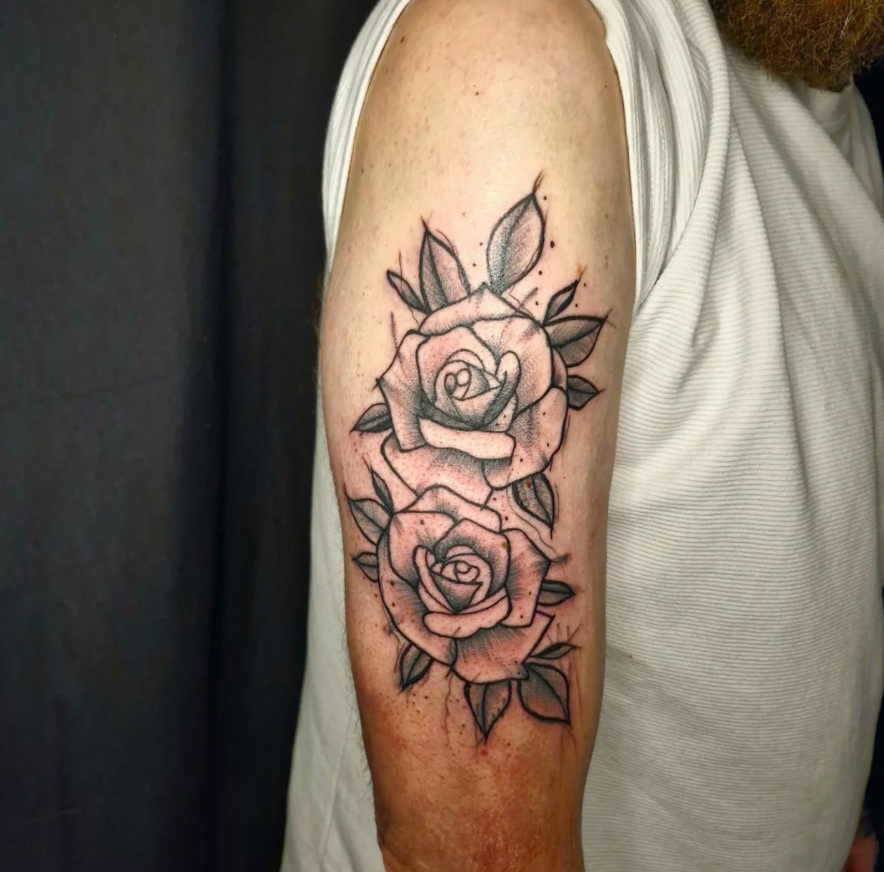 Tattoo von zwei Rosen mit Blättern am Oberarm eines Mannes, Schwarz-Weiß-Design mit feinen Linien.