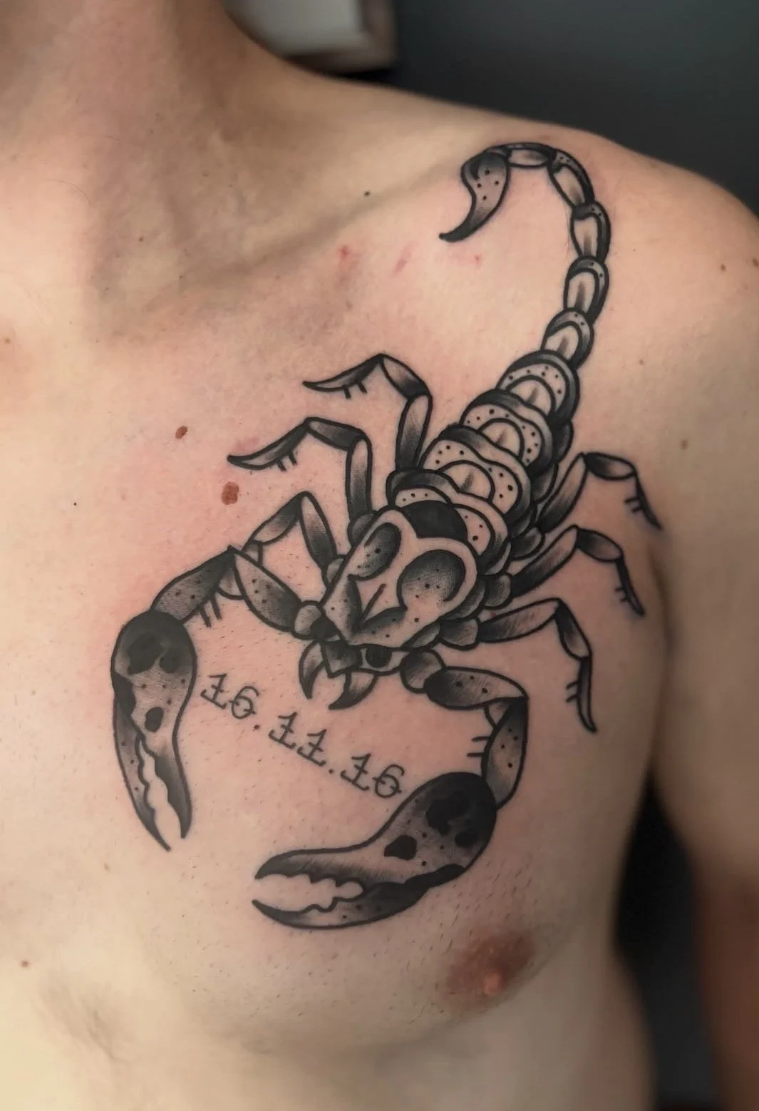 Tattoo eines Skorpions auf Brust eines Menschen, mit der Zahl 16.11.16 darunter.