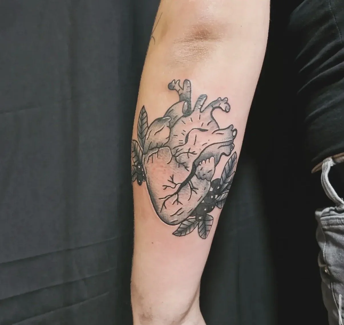 Tattoo eines menschlichen Herzens mit Blättern und Käfern auf dem Unterarm.