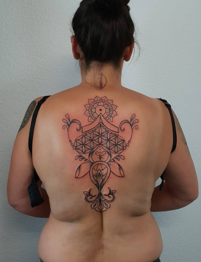 Eine Person mit einer Rückentätowierung, die geometrische und florale Muster sowie Mandala-ähnliche Designs zeigt.