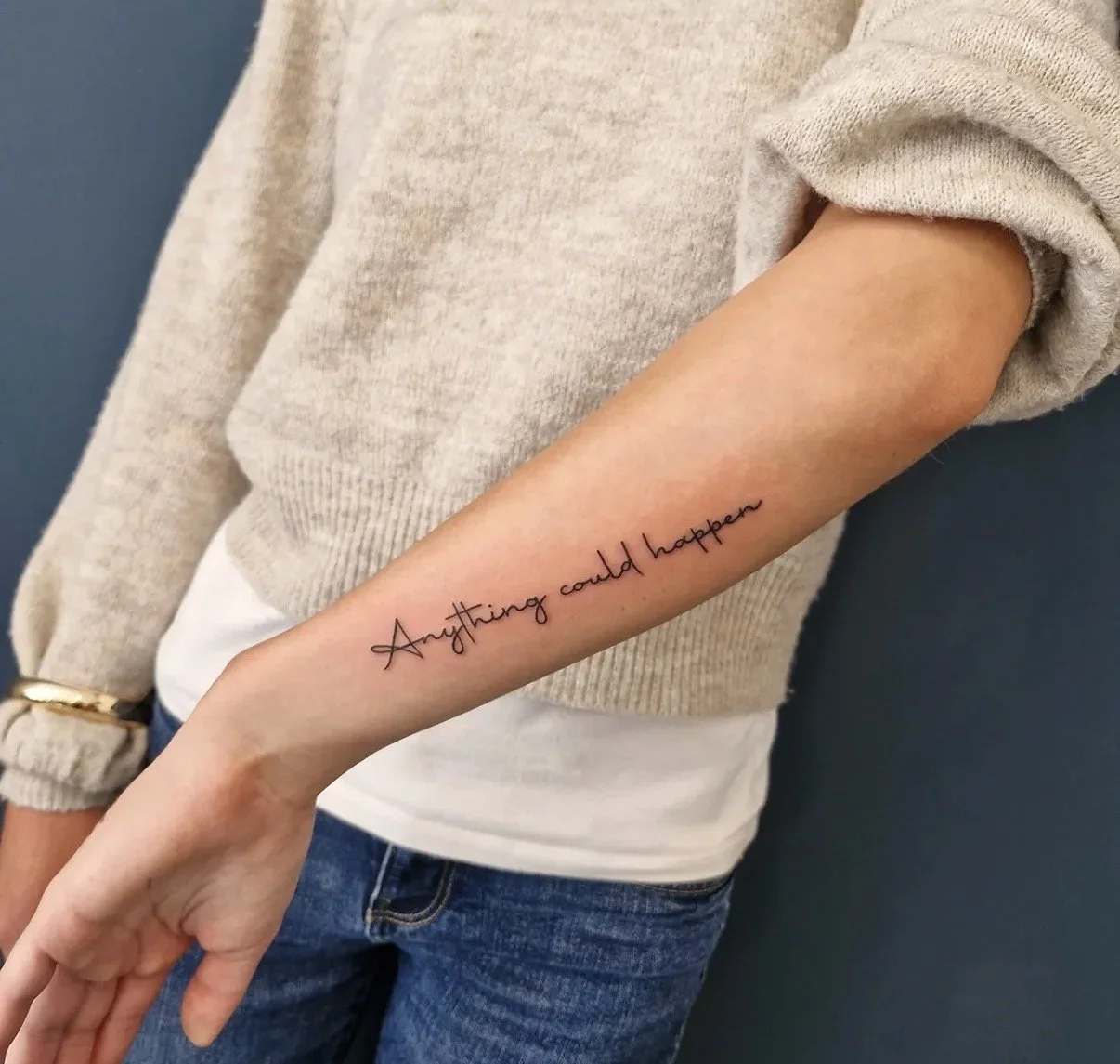 Taillierte Aufnahme eines Unterarms mit Tätowierung, auf dem in elegantem, schwarzem Schriftzug steht: "Anything could happen."