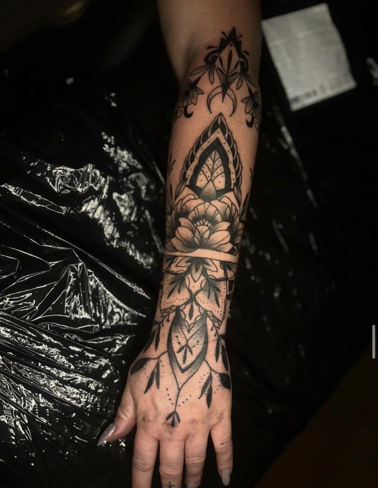 Schwarz-weiße Tätowierung eines Blumenmusters auf dem Arm, inklusive Blüten, Blätter und dekorative Elemente.