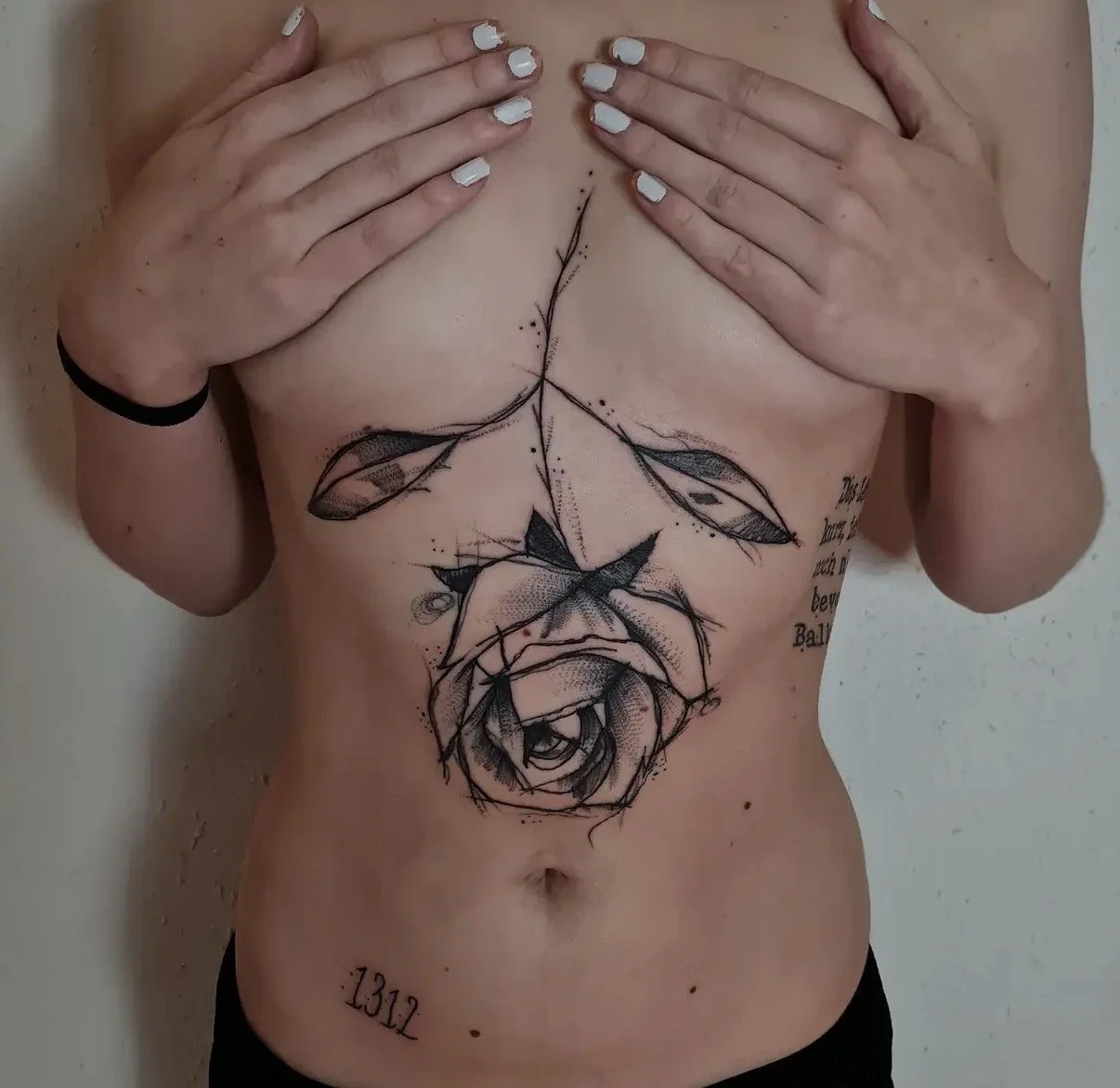 Eine Person mit einem schwarzen Gummiband am Handgelenk zeigt eine große Tattoo auf dem Bauch, das eine stilisierte Rose und Blätter in Schwarz-Weiß-Design ist.