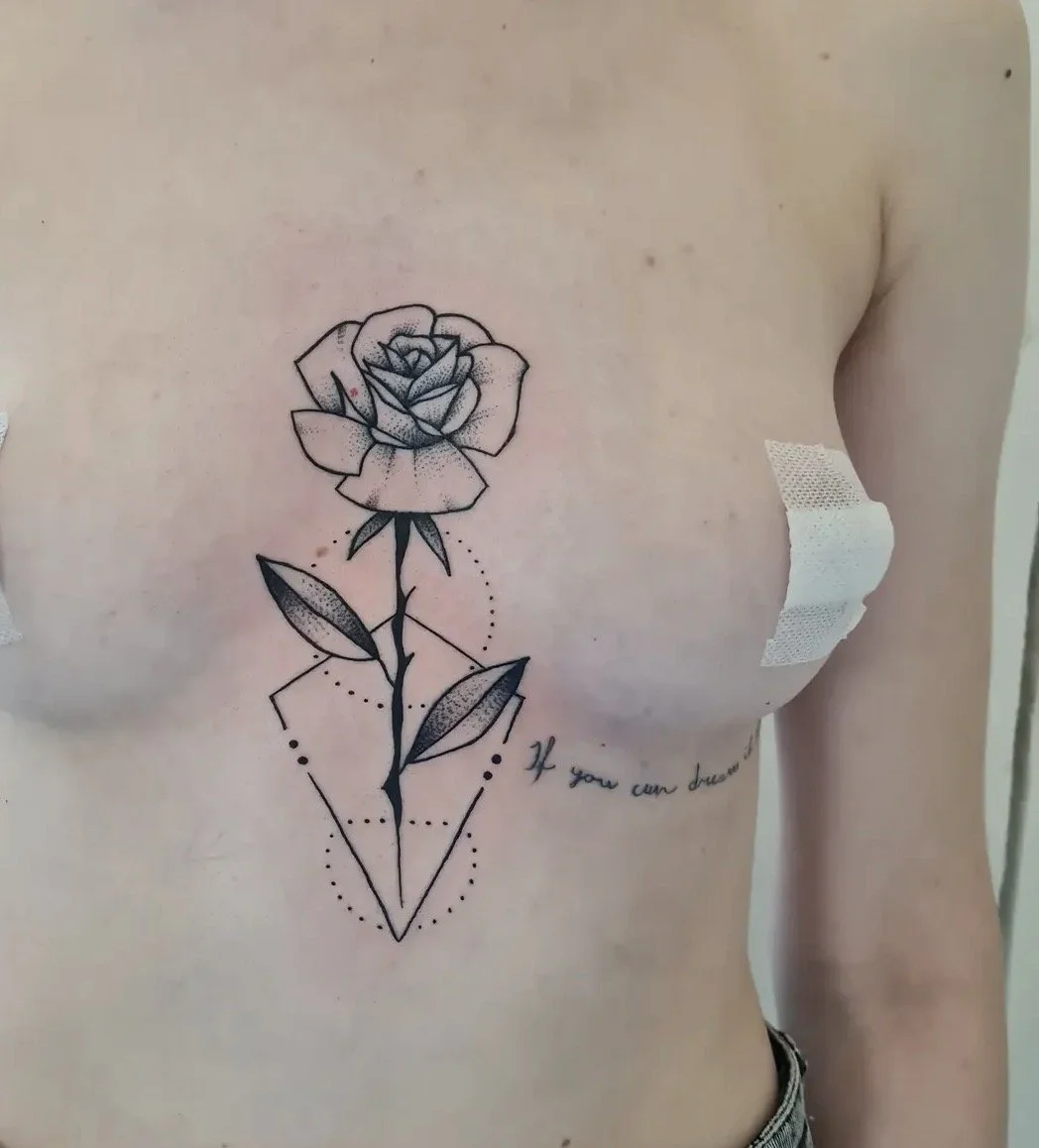 Schwarze Tattoo eines Rosenstrauchs auf der Brust einer Person, mit geometrischen Linien und Punkten, begleitet von einem Schriftzug.