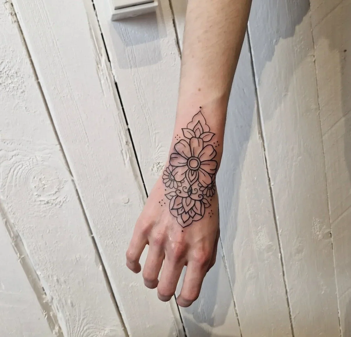 Schwarz-weiße Tattoo eines Blumenmusters am Handgelenk.