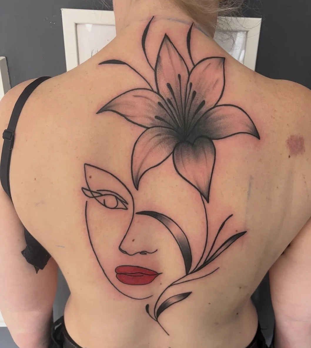 Tattoo eines Gesichtes und einer großen Lilie auf dem Rücken einer Person.