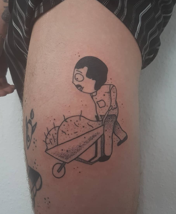 Tattoo eines Cartoon-Mädchens, das in einer Säge sitzt, auf dem Oberarm.
