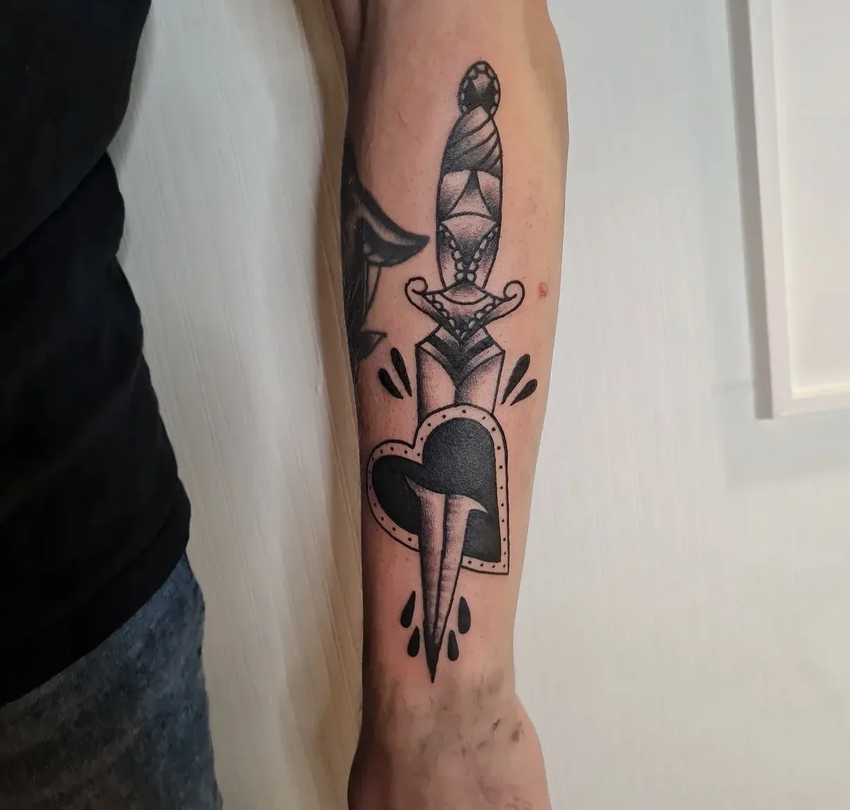 Tattoo eines Dolches in einer Herzform auf dem Unterarm.