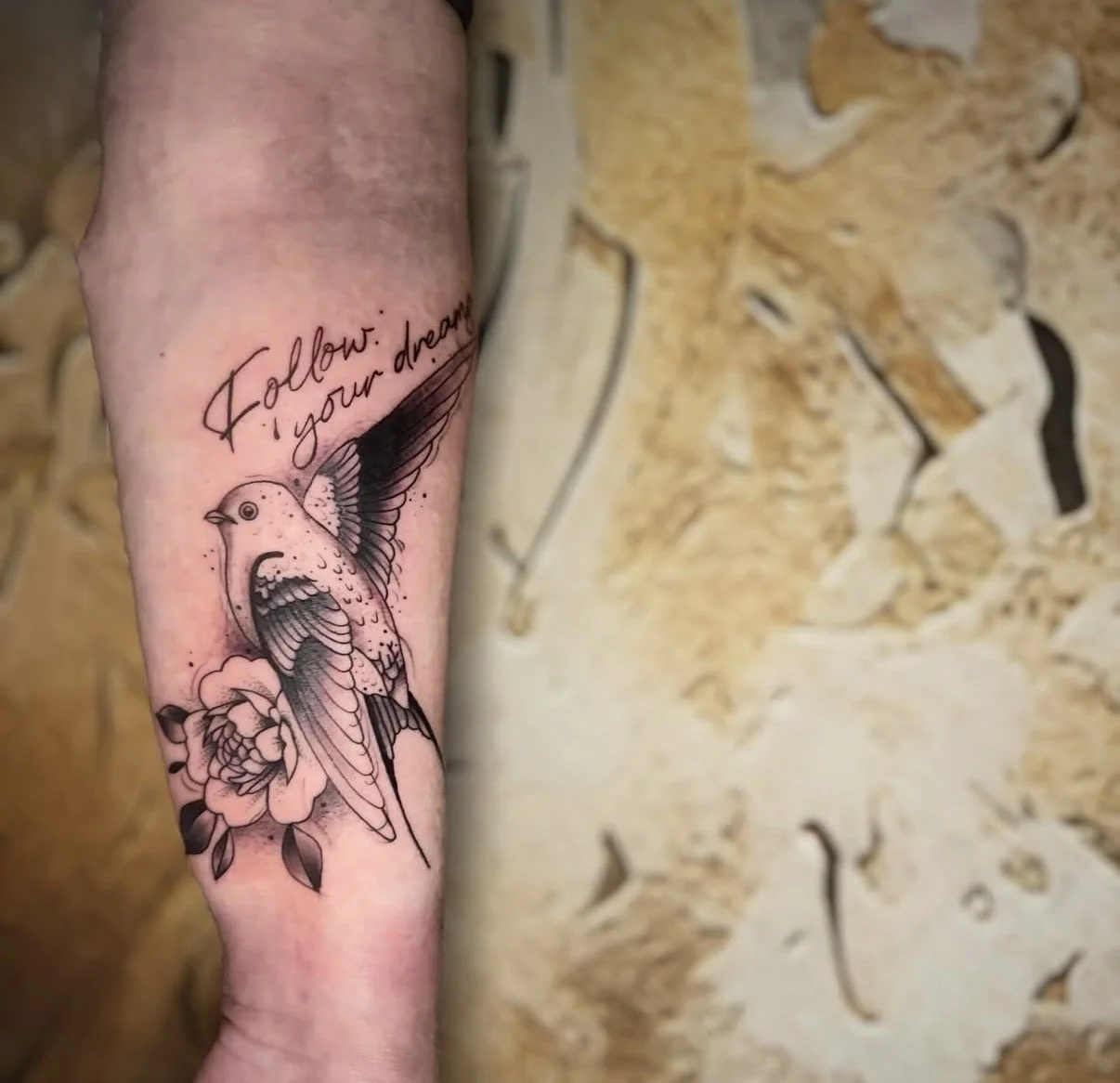Tattoo eines singenden Vogels mit einem Zitat "Follow your dream" auf dem Unterarm.