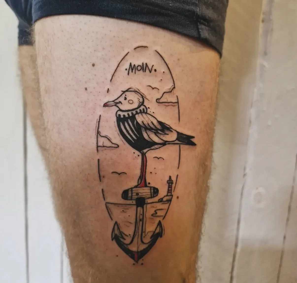 Tattoo eines Möwenkopfs mit Anker darunter, im Hintergrund Leuchtturm und Wolken, mit Text "MOIN".