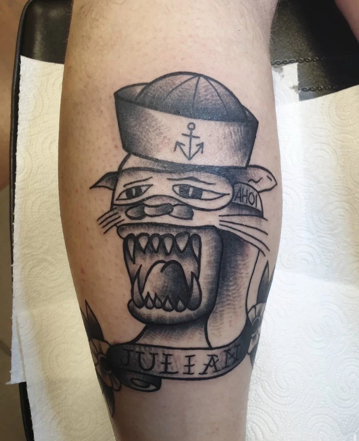 Tattoo eines knurrenden Tigers mit einem Matrosenhut, der ein Anker-Symbol trägt und den Schriftzug "QUEEN" auf dem Banner hat.