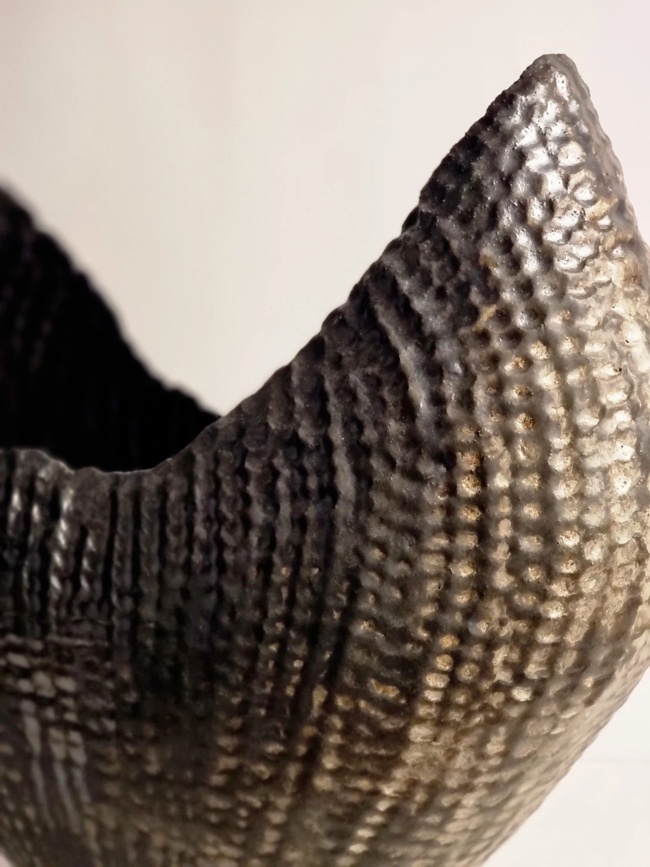 Close-up of a textured, metallic vessel  with a rough, dotted surface.