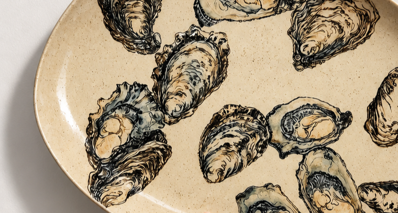 Close-up of a beige ceramic plate with black illustrations of oysters on it.