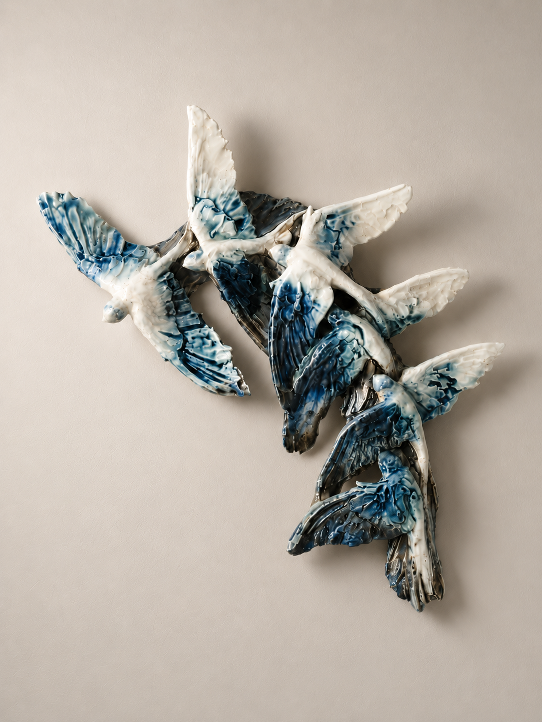 Ceramic sculpture of three flying birds with blue and white colors on a plain beige background.