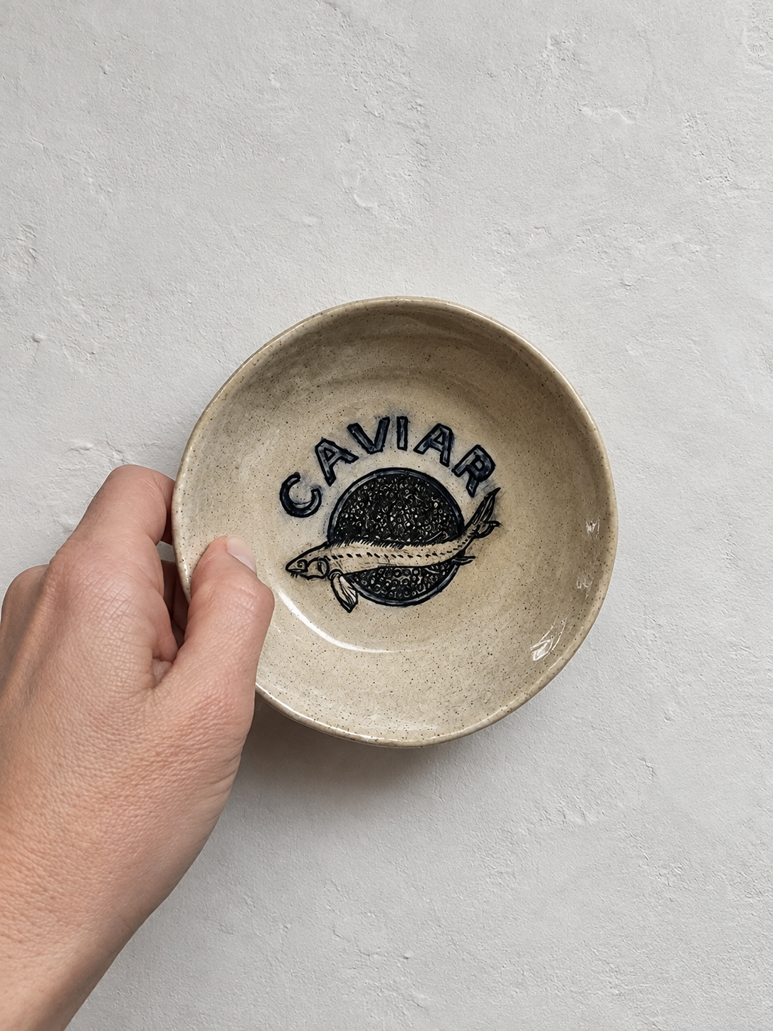 Small beige ceramic dish with an illustration of a fish.