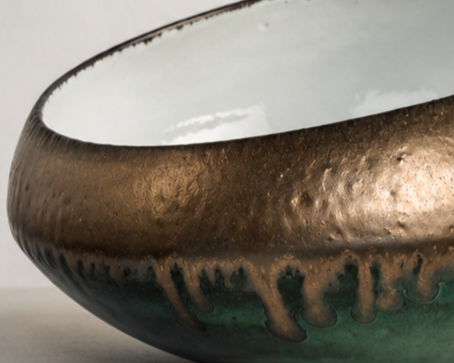 Close-up of a ceramic bowl with a glazed, textured exterior in earthy tones and a smooth, reflective interior.