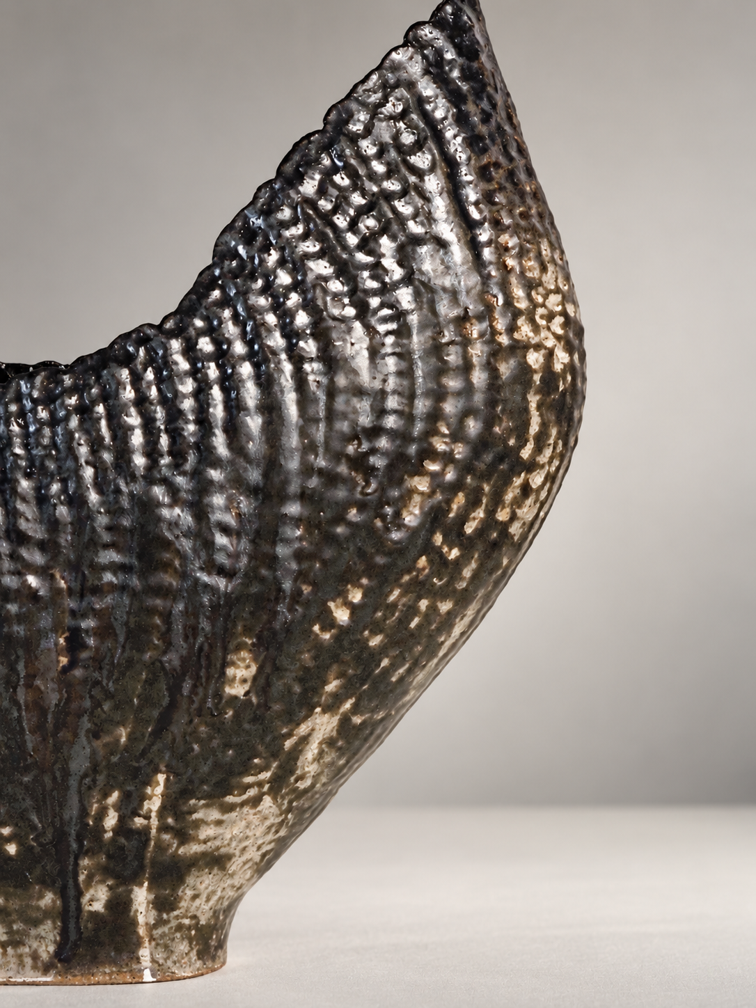 Close-up of a ceramic vessel with a textured, dark, and glossy surface, showing intricate patterns.
