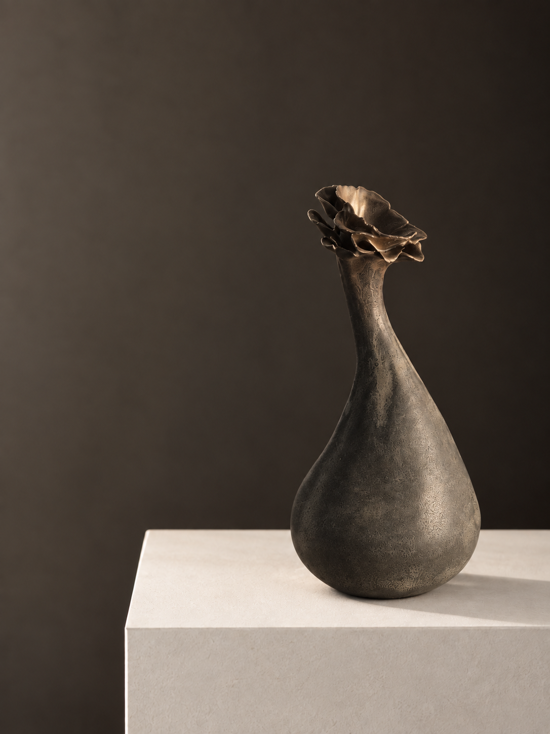 A ceramic vase with a textured surface and a flower-like top, placed on a white pedestal against a dark background.
