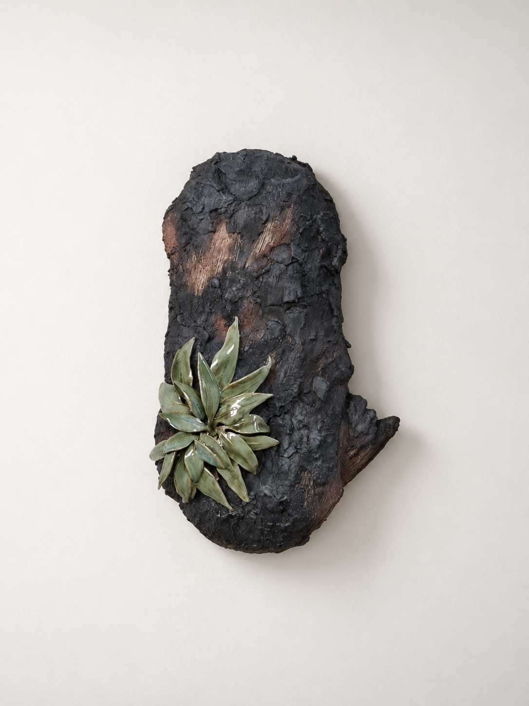 A wall sculpture resembling charred wood and green succulent plants against a white wall.