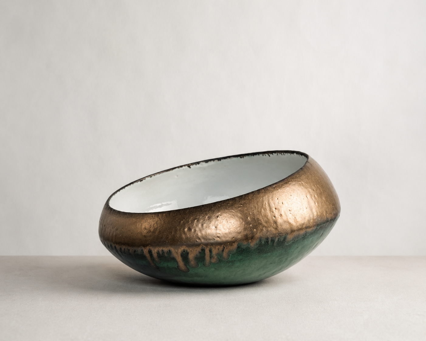 A ceramic bowl with a metallic gold upper half, green lower half, and black drip glaze, placed on a light-colored surface against a plain white background.