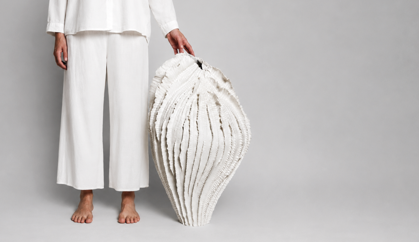 Person next to a large, white, intricately textured shell sculpture, standing barefoot against a plain gray background.