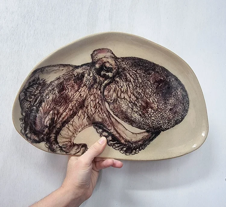 A person holding a beige bowl with a detailed drawing of an octopus.