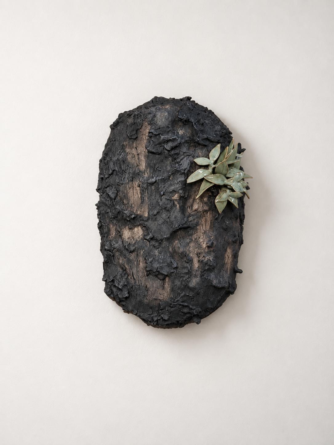 Mixed media art piece, made with textured black material and green ceramic leaves on a white background.