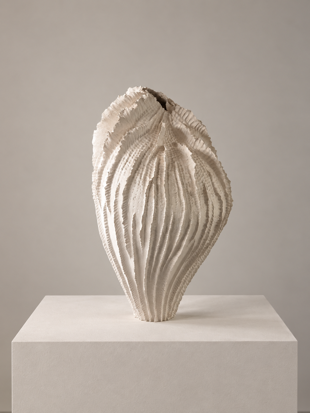 White sculptural art piece with intricate textured ridges, displayed on a white pedestal against a plain gray background.