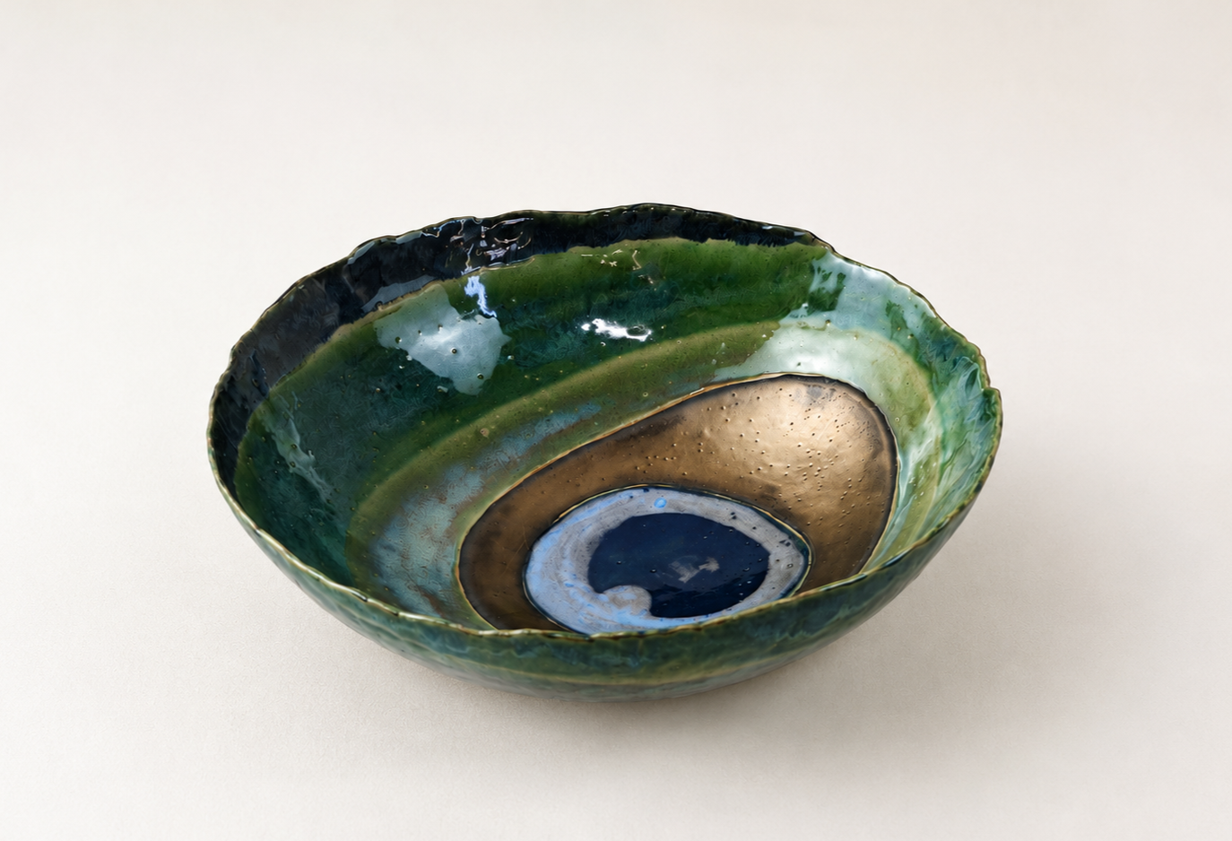 Handmade glass bowl with green, blue, gold, and black swirling patterns, placed on a plain white surface.