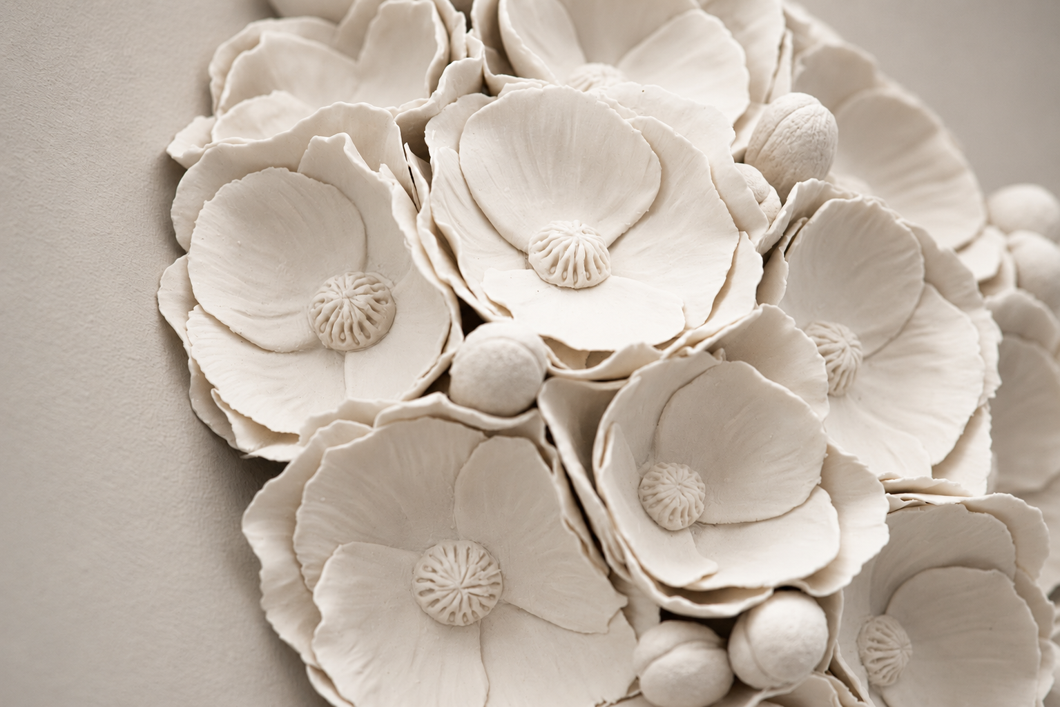 A close-up of a decorative arrangement of cream-colored ceramic flowers and round buds with detailed petals and centers.