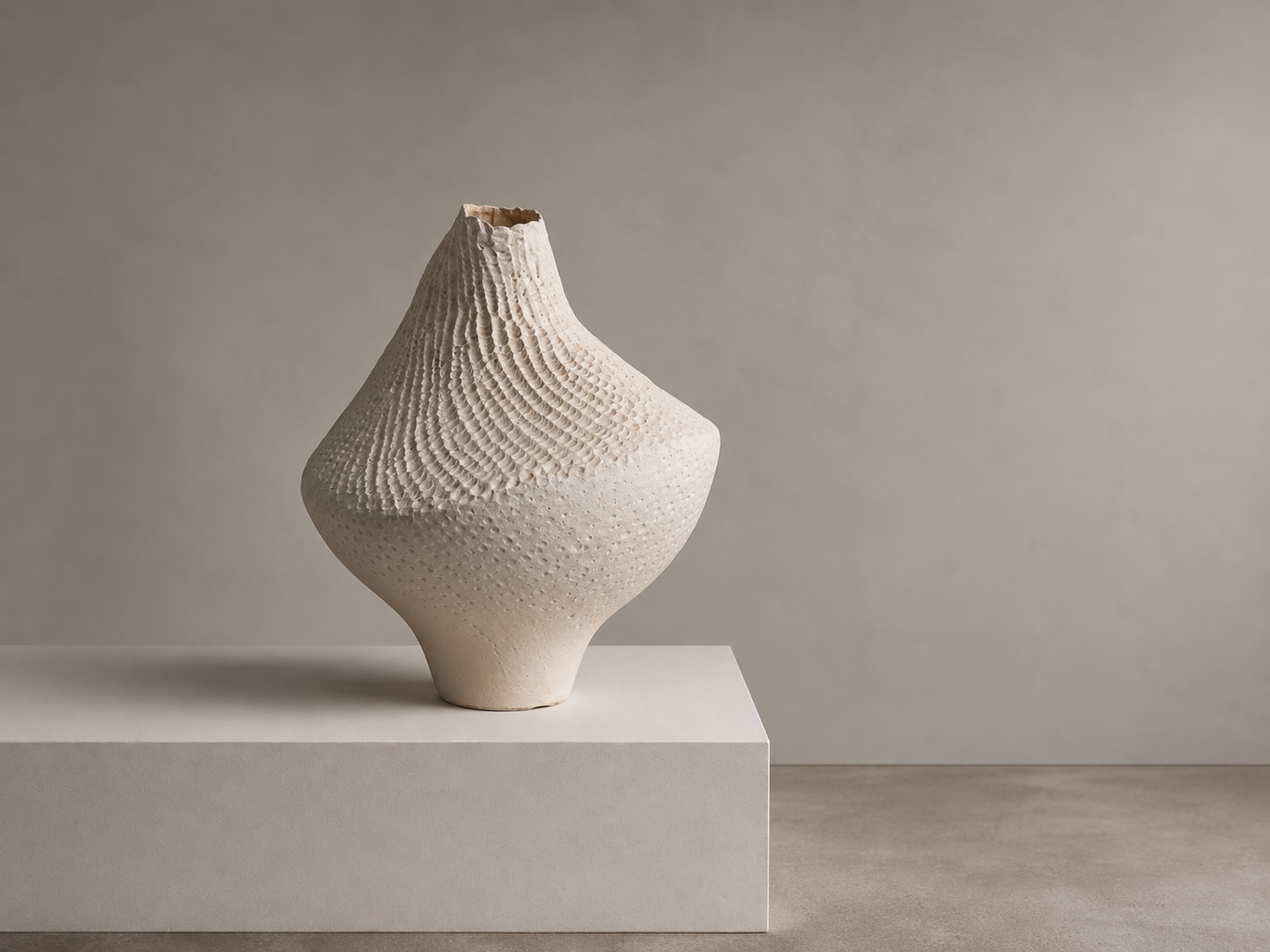 Decorative beige ceramic vase with textured patterns, positioned on a white pedestal against a neutral backdrop.