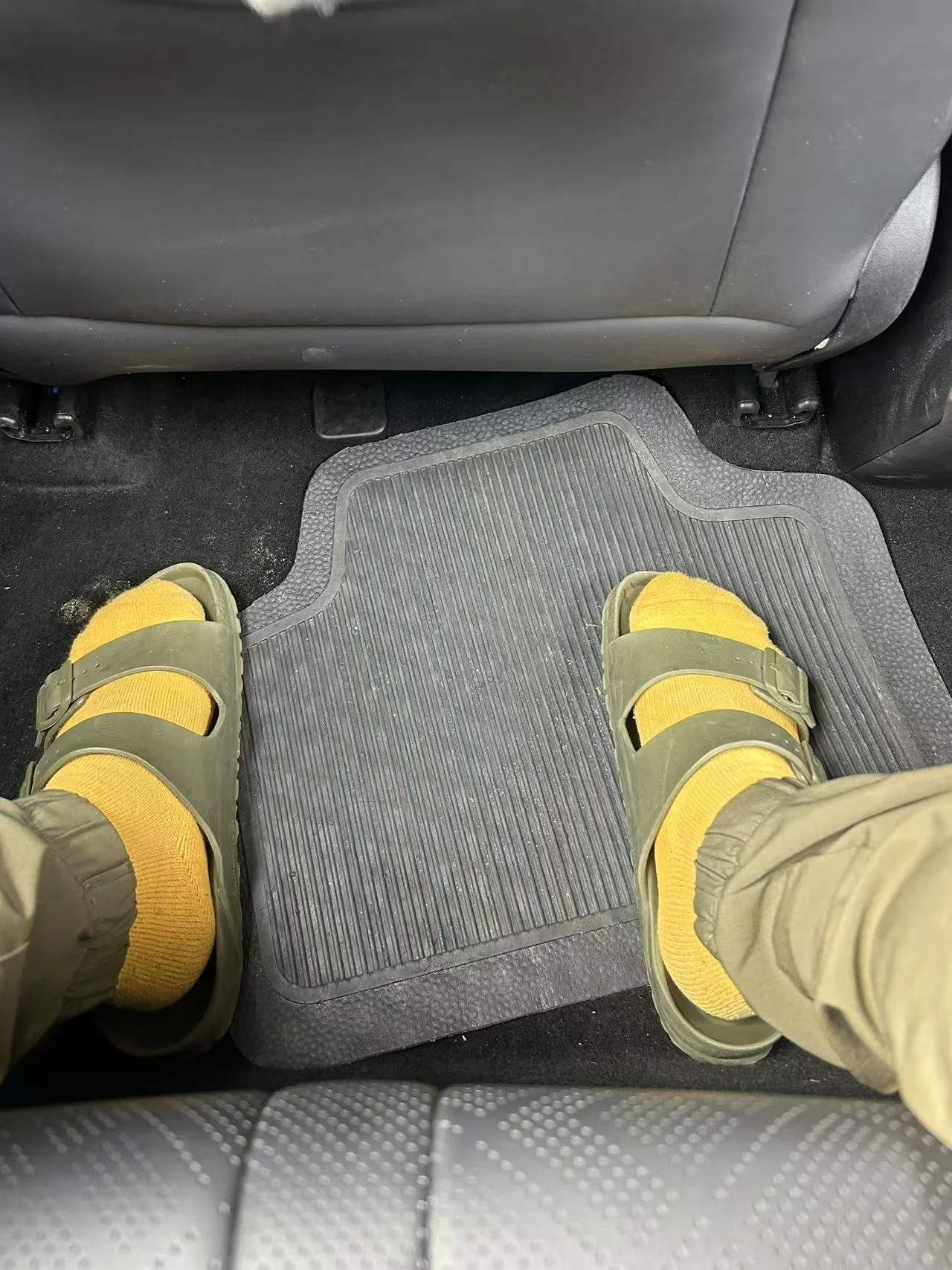 Person wearing yellow socks and green sandals standing on a rubber car floor mat inside a vehicle.