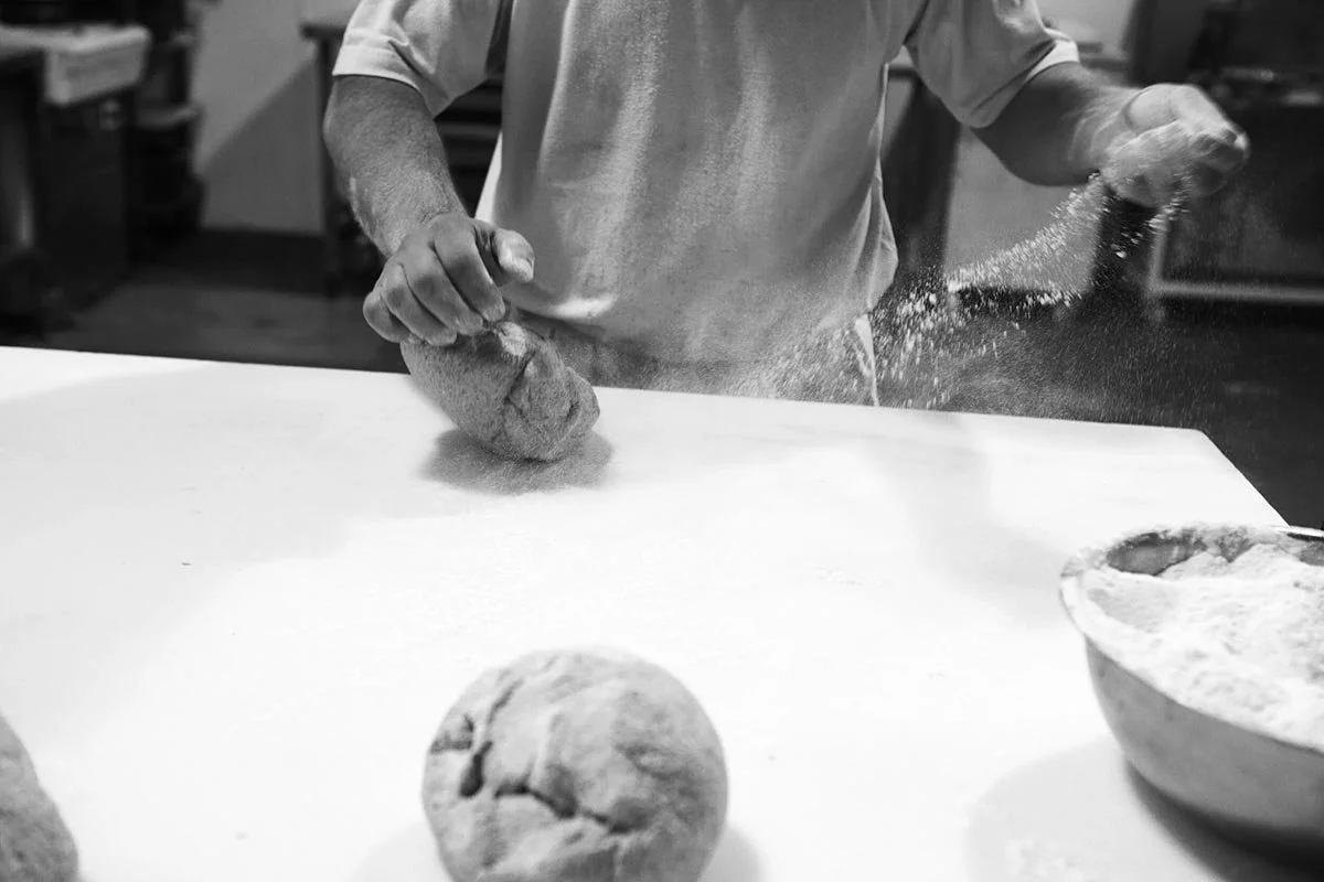 Person kneading dough on a countertop in a bakery or kitchen.