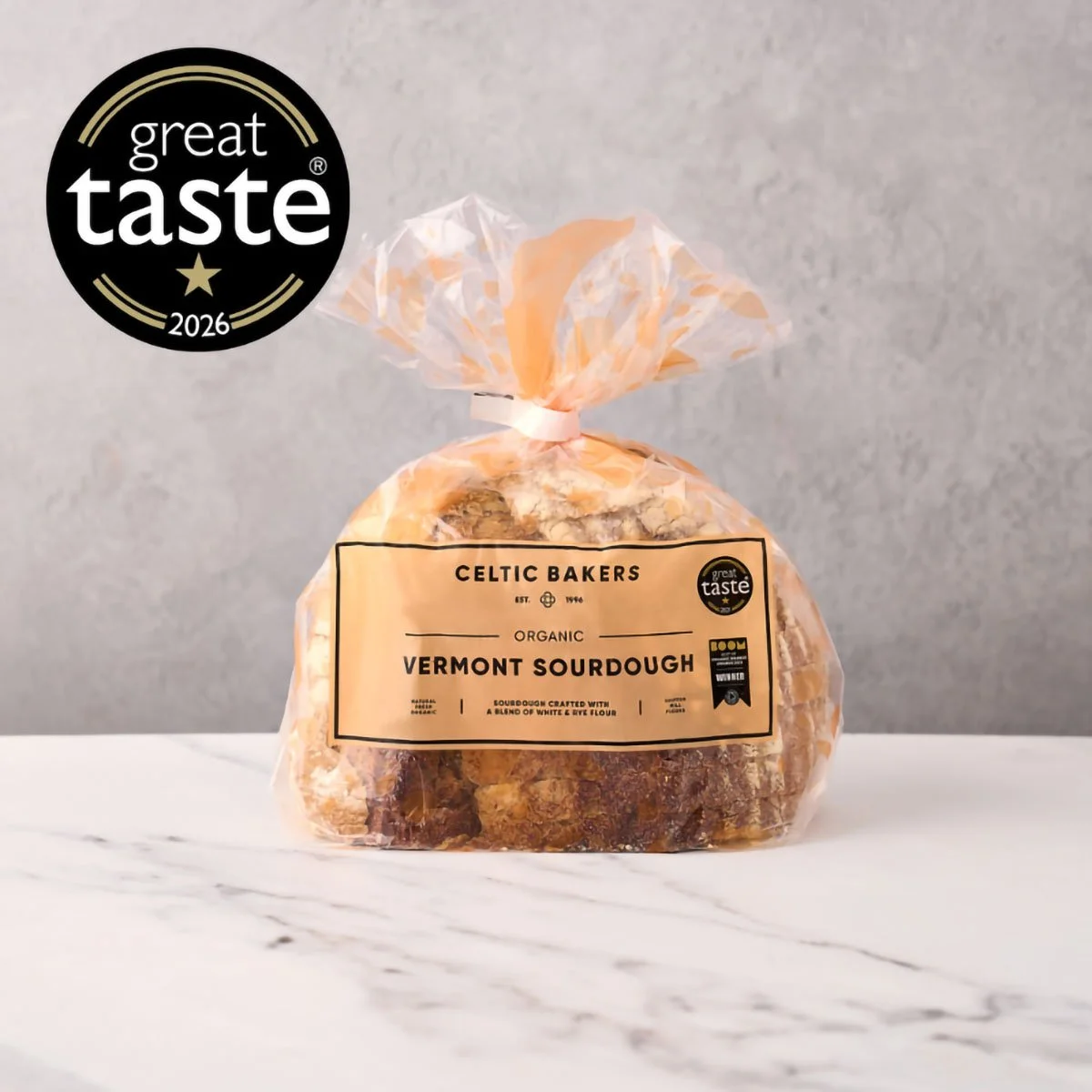 Clear plastic bag of Celtic Bakers organic Vermont sourdough bread, with a beige label, placed on a marble surface against a gray wall.