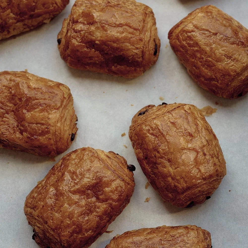 Close-up of several golden-brown, flaky, rectangular puff pastries with some visible dark spots, resting on white parchment paper.