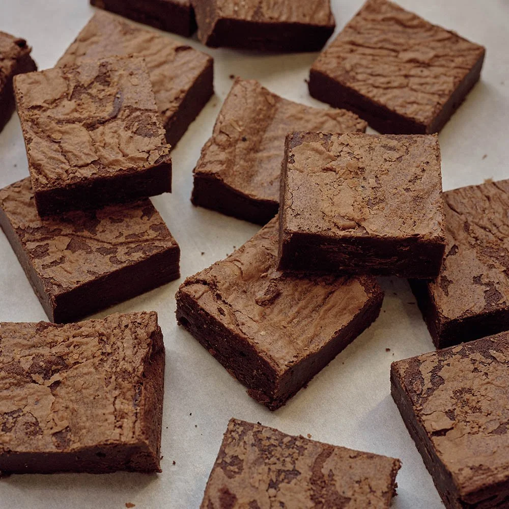 Several pieces of chocolate brownies with cracked tops on a sheet of paper.